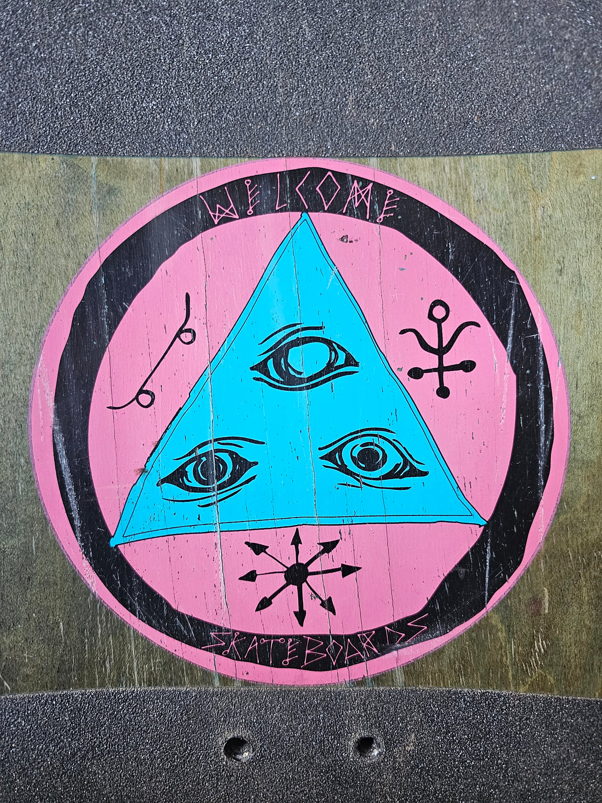 Close-up of scratched Welcome three-eye triangle emblem on exposed top woodgrain